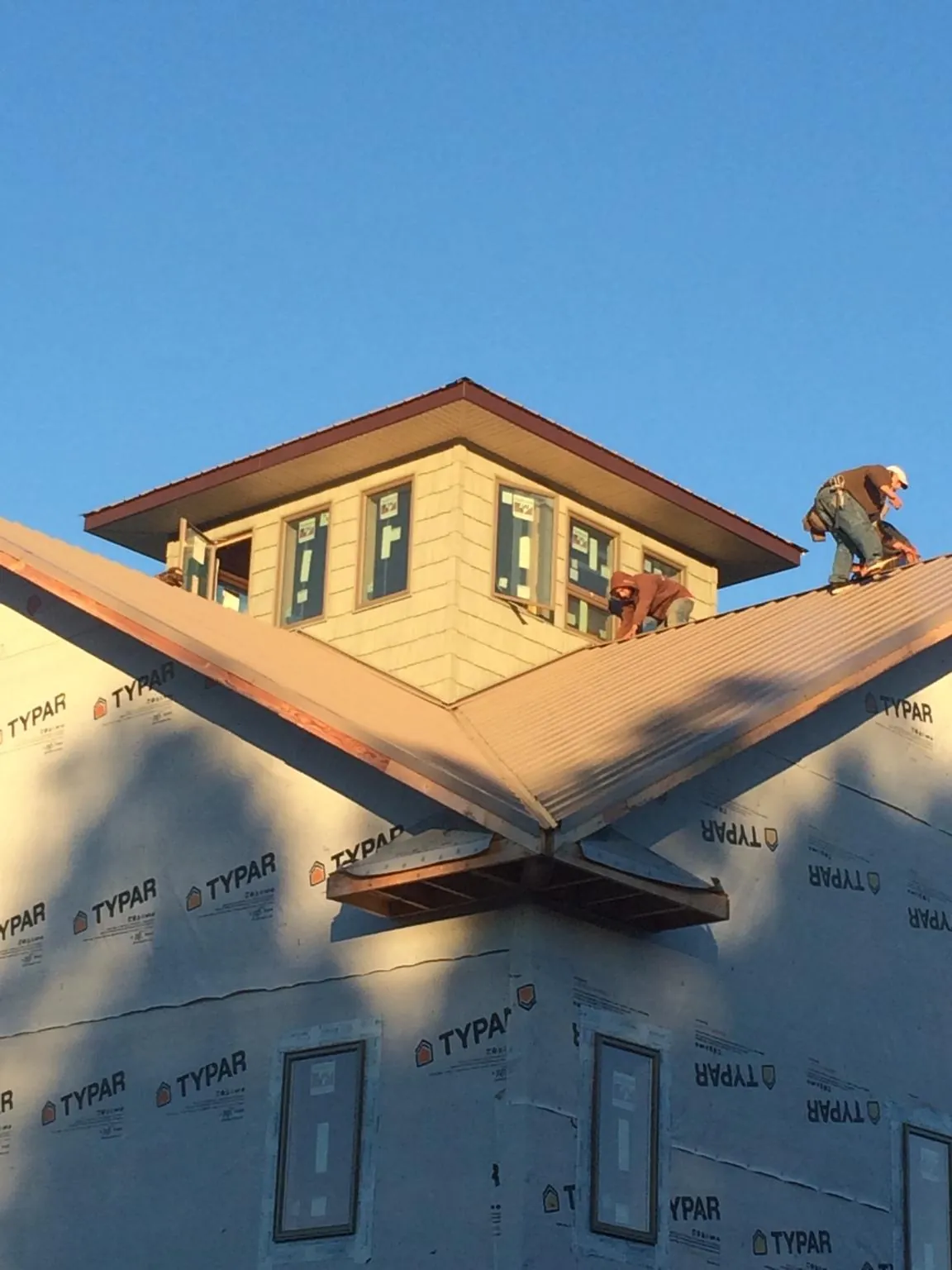 Roofers working around a rooftop cupola on a new metal roof at sunset in Northfield